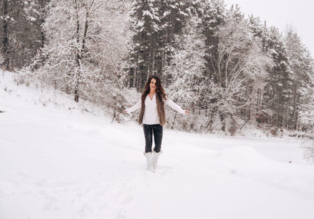 woman in white standing in snow with white boots black pants and white shirt